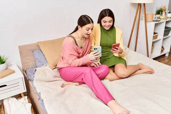 Two women, casually dressed, sitting on a bed, engrossed in a cell phone. — Stock Photo