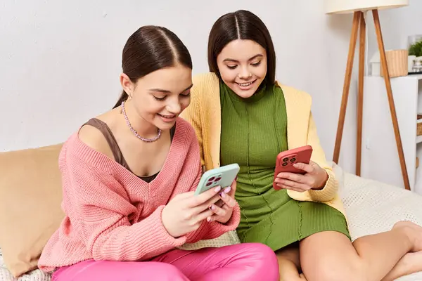 Дві молоді жінки, друзі, сидять на дивані, занурені в мобільні телефони, не знаючи про світ навколо них. — стокове фото