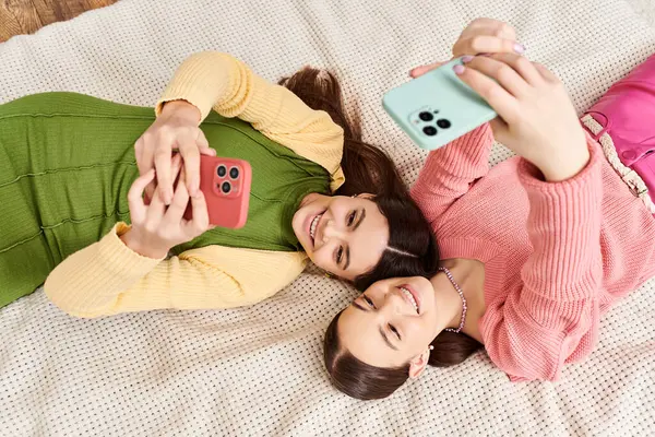 Две молодые женщины в повседневной одежде наслаждаются моментом расслабления, лежа бок о бок на уютной кровати. — стоковое фото
