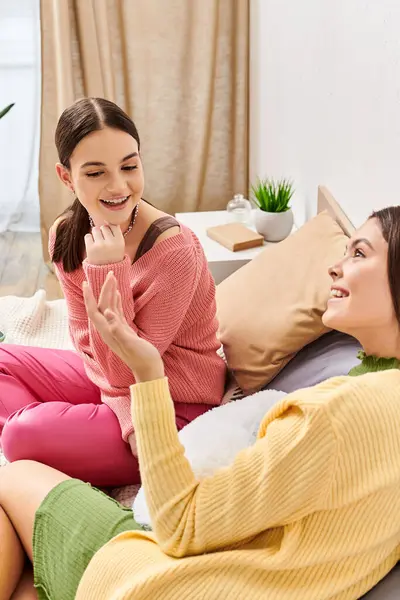 Two pretty teenage girls in casual attire, female friends, sit on a bed, engrossed in a heartfelt discussion. — Stock Photo