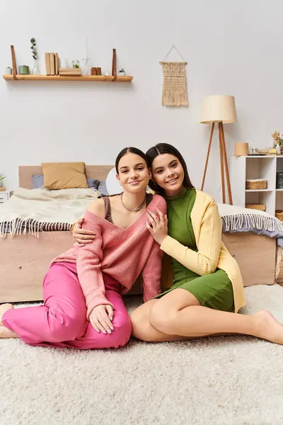 Two pretty teenage girls in casual attire sit on the floor hugging each other in a heartwarming display of friendship and companionship. — Stock Photo