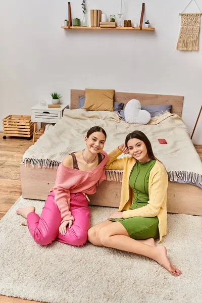 Two pretty teenage girls in casual attire sitting on the floor in front of a bed, chatting and relaxing together at home. — Stock Photo