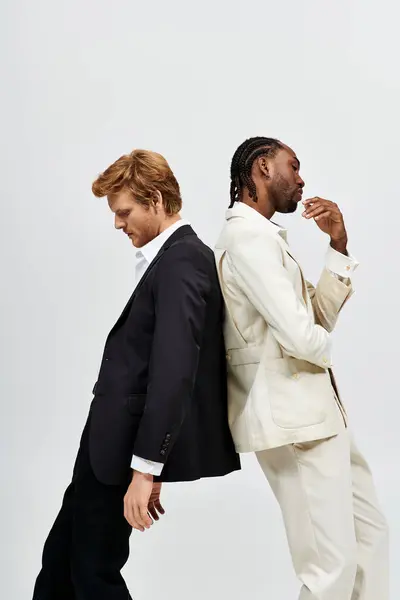 Dos hombres multiculturales en trajes elegantes posan uno al lado del otro. - foto de stock