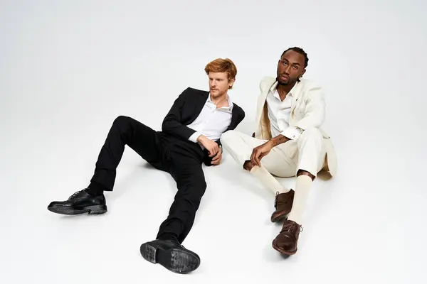 Two multicultural men in elegant dapper style sitting together on a white background. — Stock Photo