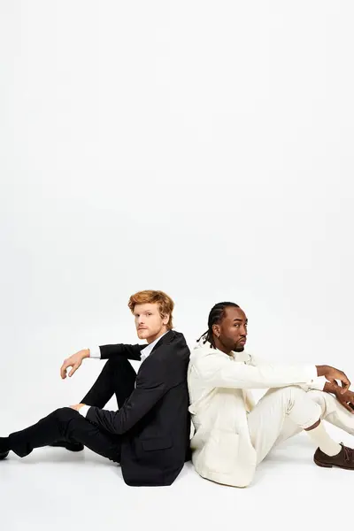 Two multicultural men with dapper style sit together on the ground. — Stock Photo