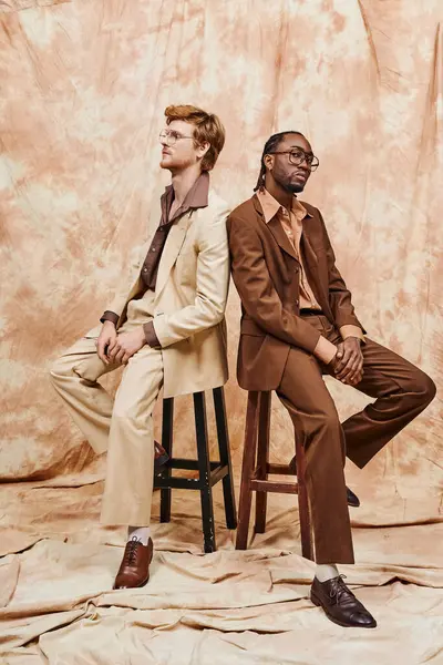 Two diverse men with dapper style sitting on top of a wooden stool. — Stock Photo