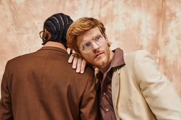 Two multicultural men dressed in dapper style hug in front of a wall. — Stock Photo