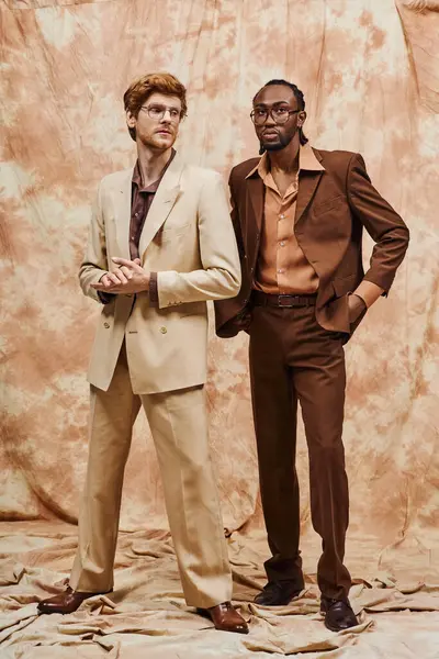 Dos elegantes hombres multiculturales se paran uno al lado del otro frente a un elegante telón de fondo. - foto de stock
