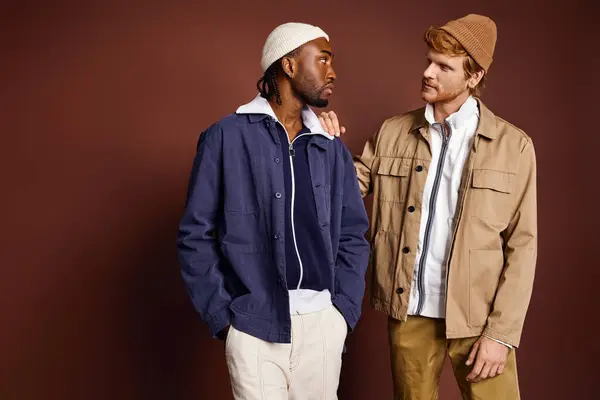 Zwei stylische multikulturelle Männer posieren elegant vor einer braunen Wand. — Stockfoto