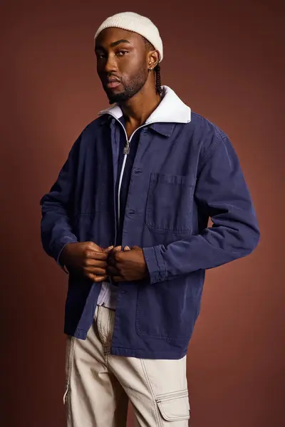 Un joven afroamericano guapo con chaqueta azul y sombrero blanco. - foto de stock