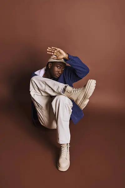 Handsome African American man in stylish outfit sitting on the ground with hands on head. — Stock Photo