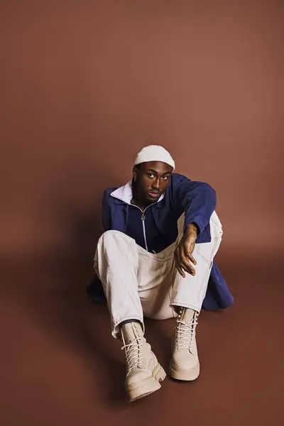 Handsome young African American man in stylish outfit sitting cross-legged on the ground. — Stock Photo