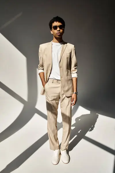 Handsome African American man in beige suit and stylish sunglasses standing in front of white wall. — Stock Photo
