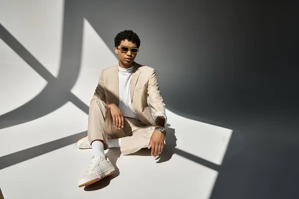 African American man in beige suit sitting comfortably on the floor, wearing stylish sunglasses. — Stock Photo