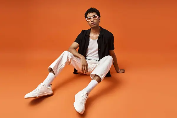 Stylish man in sunglasses and white pants on orange background. — Stock Photo