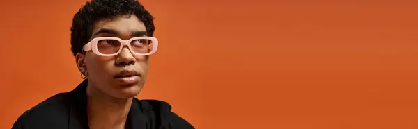 Handsome African American man in pink glasses against orange backdrop. — Stock Photo
