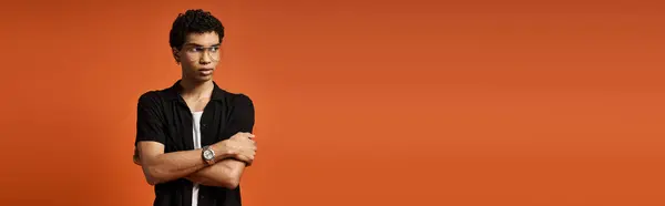Stylish African American man with arms folded in front of bold orange backdrop. — Stock Photo
