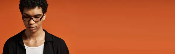 Handsome African American man in stylish sunglasses standing confidently against bright orange background. — Stock Photo