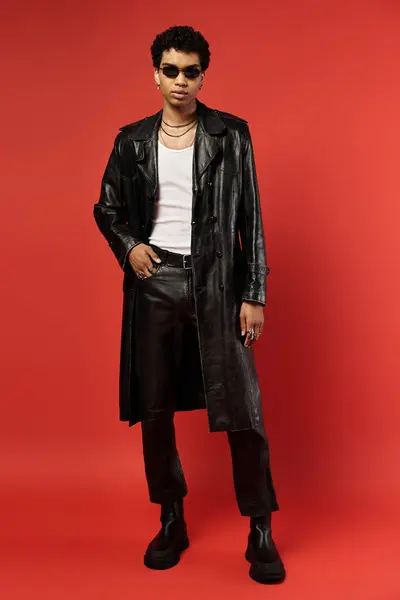 Bonito homem afro-americano em casaco de couro preto posando contra fundo vermelho. — Fotografia de Stock