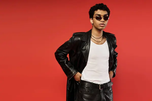 Stylish man in leather jacket and white shirt strikes a pose against vibrant red backdrop. — Stock Photo
