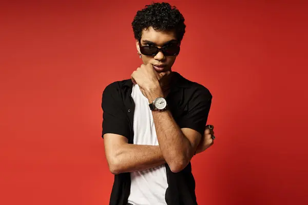 Jovem afro-americano com óculos de sol marcando uma pose com relógio contra fundo vermelho. — Fotografia de Stock