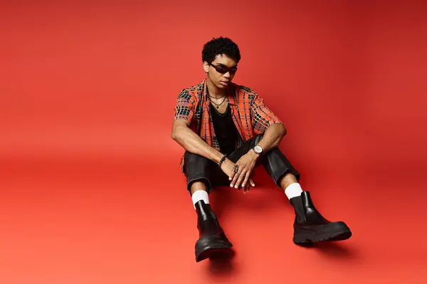 Handsome man in red shirt and black boots sitting on red background. — Stock Photo