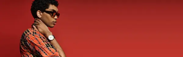 Handsome African American man striking a pose in stylish sunglasses against a bold red backdrop. — Stock Photo