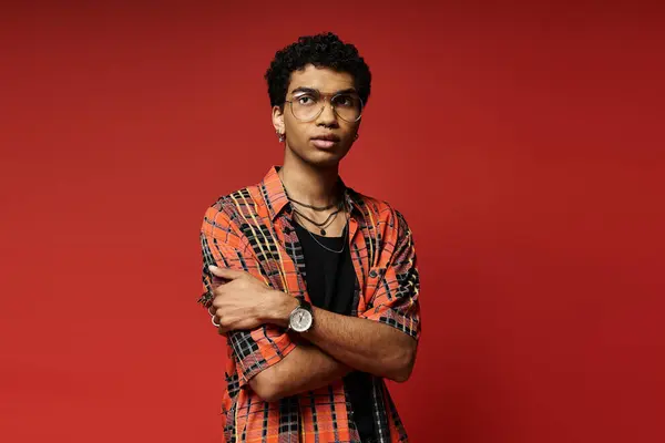 Handsome young man posing confidently in plaid shirt against vibrant red backdrop. — Stock Photo