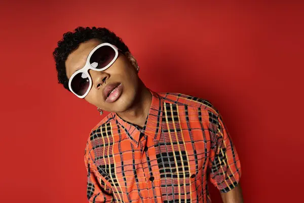 Bonito homem afro-americano em camisa xadrez e óculos de sol em fundo vermelho vibrante. — Fotografia de Stock