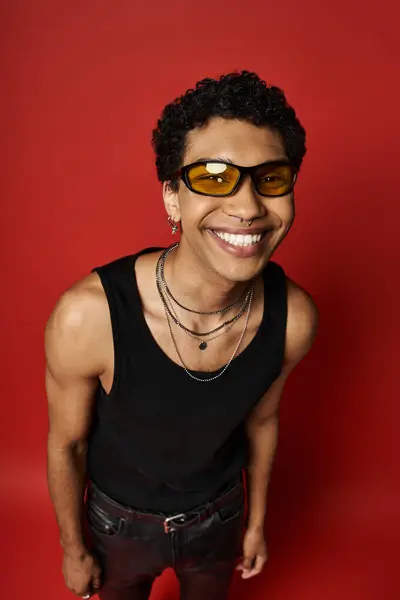 A smiling African American man wearing stylish sunglasses against a vibrant red background. — Stock Photo