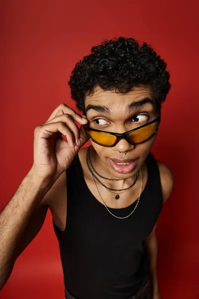 A young man exudes cool vibes in sunglasses against a bold red backdrop. — Stock Photo