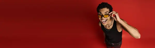 Beau Afro-Américain avec des lunettes de soleil se tient devant un fond rouge audacieux. — Photo de stock