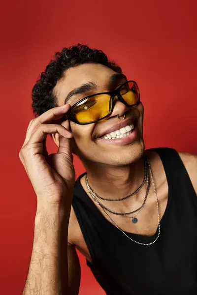 Bonito afro-americano em óculos de sol sorrindo contra vibrante fundo vermelho. — Fotografia de Stock