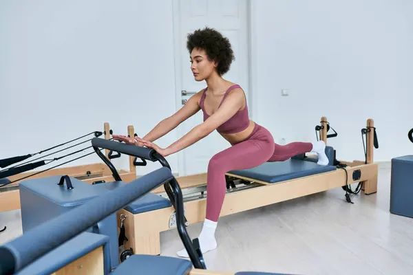 Fit mulher em sutiã esportivo rosa e leggings exercendo em uma máquina estacionária. — Fotografia de Stock