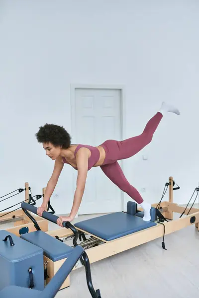 Mujer afroamericana en rosa, entrenamiento de máquina de remo. - foto de stock