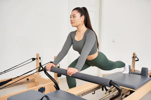 Una mujer deportiva con camisa gris, pantalones verdes en la lección de Pilates. - foto de stock