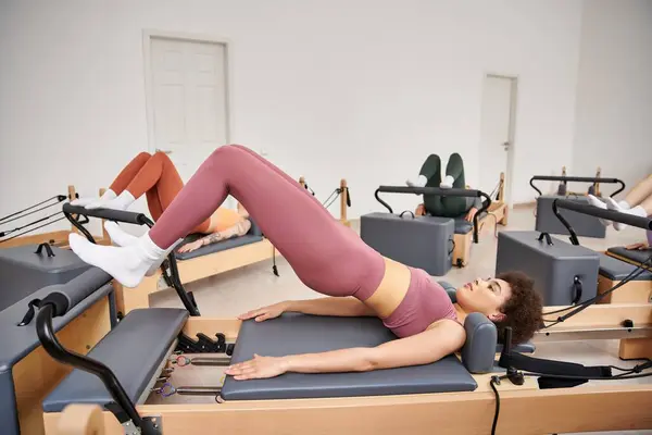 Diversas mujeres deportivas, que participan en una lección de pilates en varios equipos de ejercicio. - foto de stock