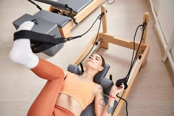 A sporty woman laying on a stationary exercise machine during a pilates lesson. — Stock Photo