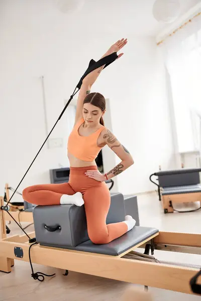 Une femme sportive en haut orange et pantalon lors d'une leçon de Pilates. — Photo de stock