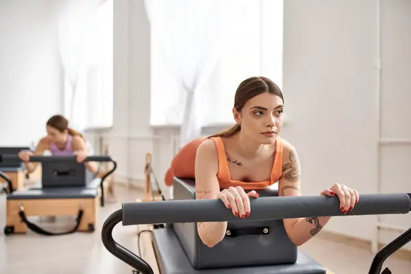 Una mujer deportista haciendo ejercicio durante una clase de pilates, junto a su amiga. - foto de stock