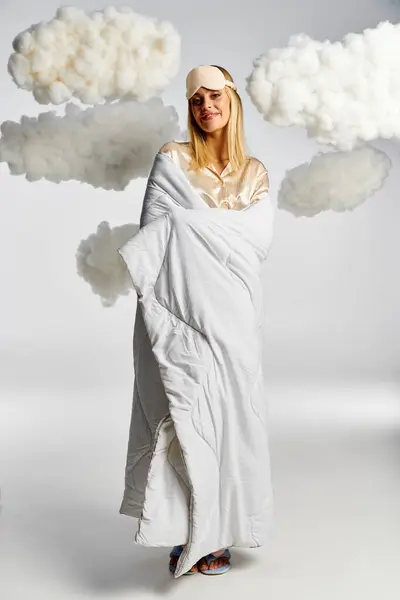 Eine verträumte blonde Frau in einer weißen Decke, umgeben von flauschigen Wolken. — Stockfoto
