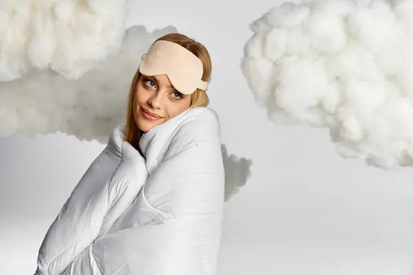 Mujer bastante soñadora cubierta con una manta blanca rodeada de nubes esponjosas. - foto de stock