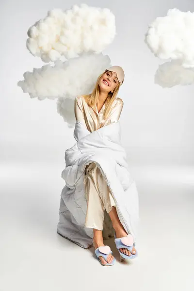 Eine verträumte blonde Frau im kuscheligen Pyjama sitzt friedlich inmitten flauschiger Wolken. — Stockfoto