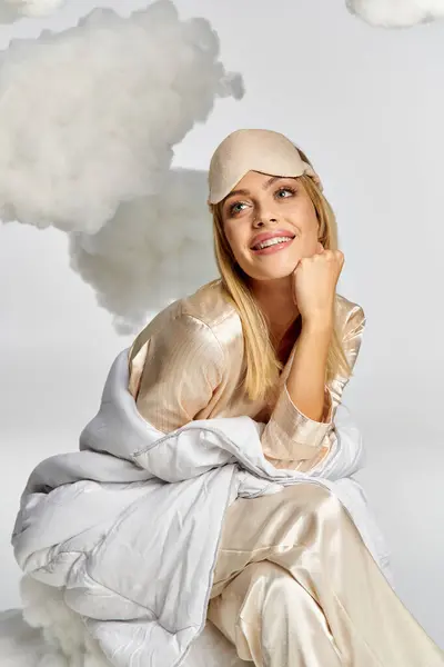 Une femme blonde rêveuse en pyjama confortable est assise gracieusement sur un nuage de fumée gonflant. — Photo de stock