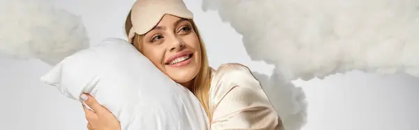 Eine blonde Frau im kuscheligen Pyjama hält ein Kissen inmitten von Wolken. — Stockfoto