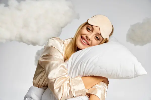 Eine schöne blonde Frau im kuscheligen Pyjama lächelt, während sie ein Kopfkissen hält. — Stockfoto