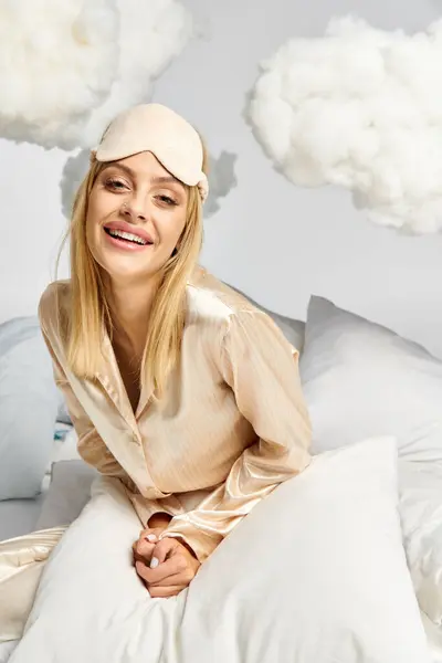 Une femme blonde rêveuse en pyjama confortable se trouve au sommet d'un oreiller blanc au milieu de nuages moelleux. — Photo de stock