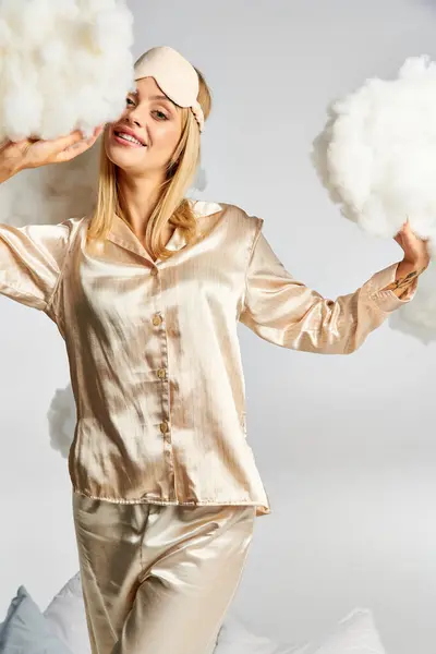 Femme blonde en pyjama doré entourée de nuages duveteux. — Photo de stock