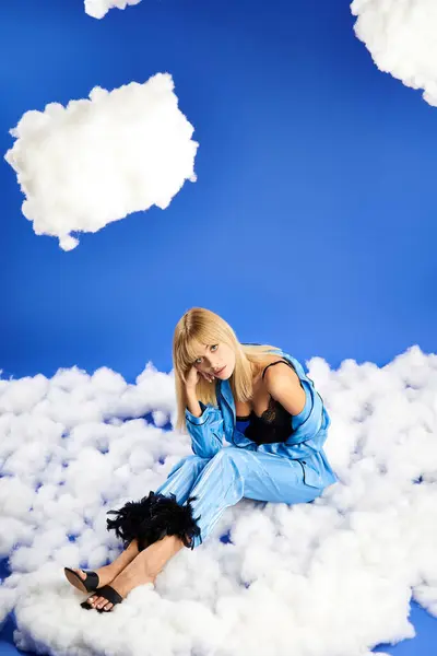 Blonde Frau in lebendiger Kleidung sitzt anmutig auf flauschigem, wolkenverhangenem Himmel. — Stockfoto