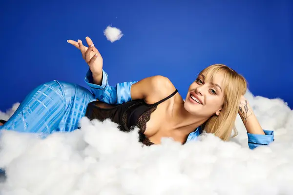 A mesmerizing blonde woman in vibrant attire lounging on a bed of clouds in the sky. — Stock Photo